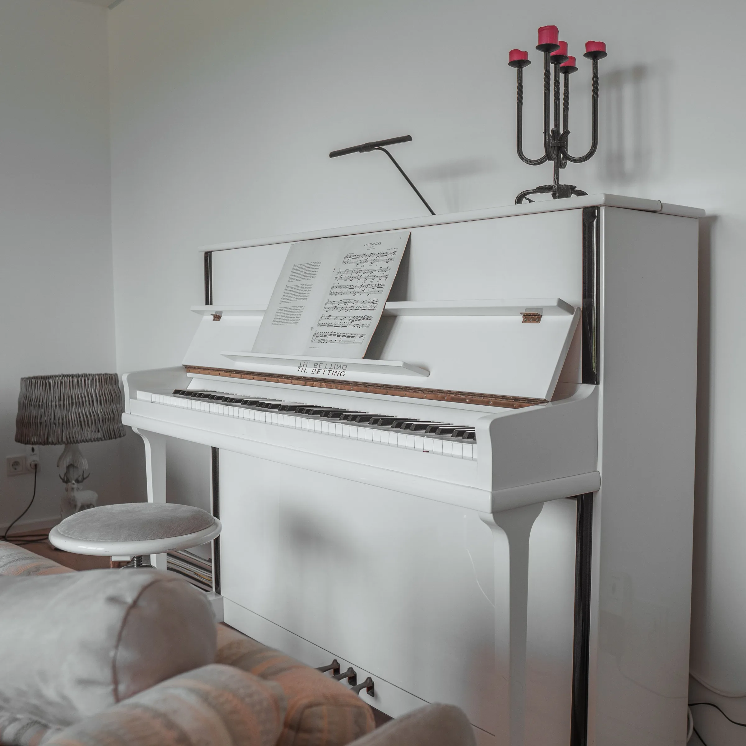 White grand piano with sheet music, candelabra, and desk lamp in a bedroom setting.